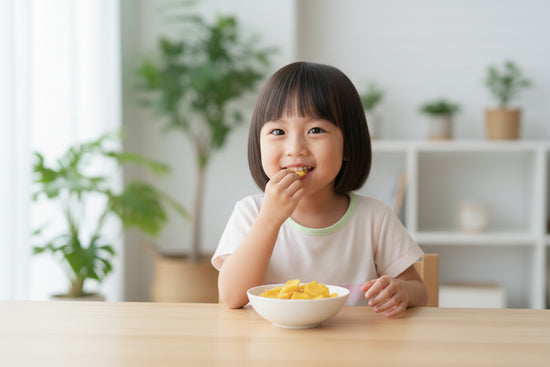 Child eating a slice of a Freeze Dried Mango from a bowl at a table with a bright, indoor setting.
